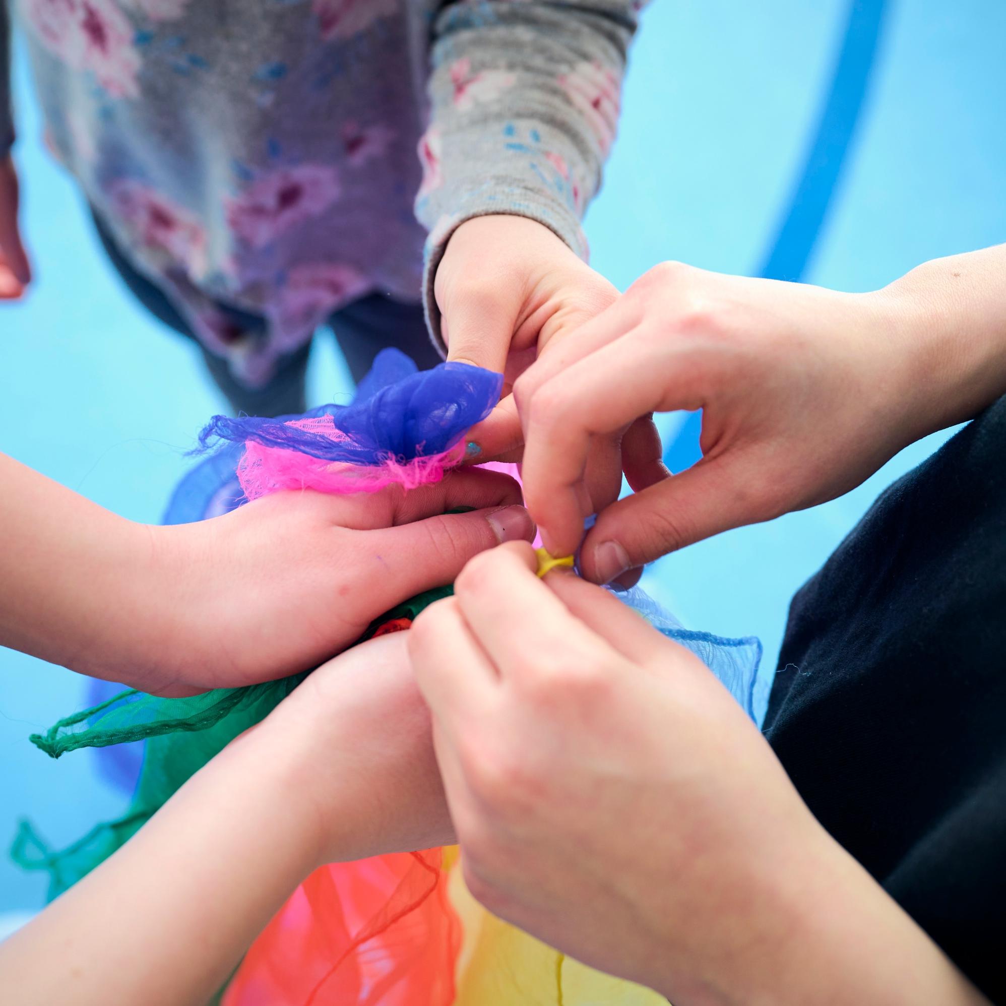 Fünf Hände halten gemeinsam ein buntes Tuch