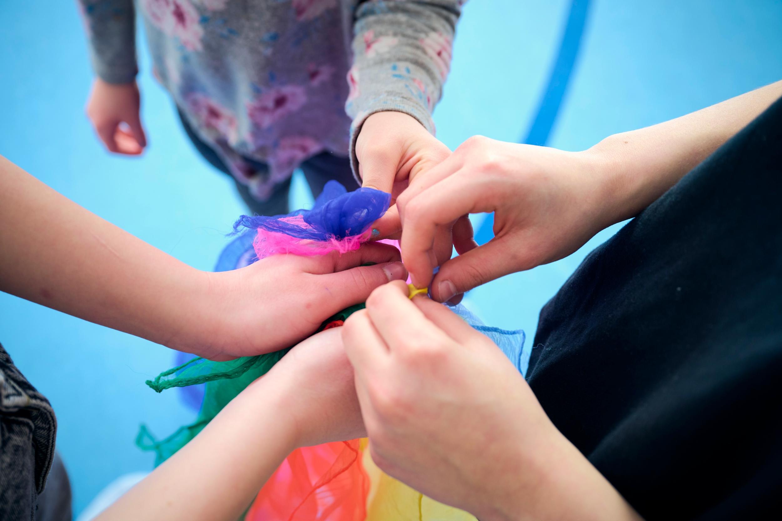 Fünf Hände halten gemeinsam ein buntes Tuch